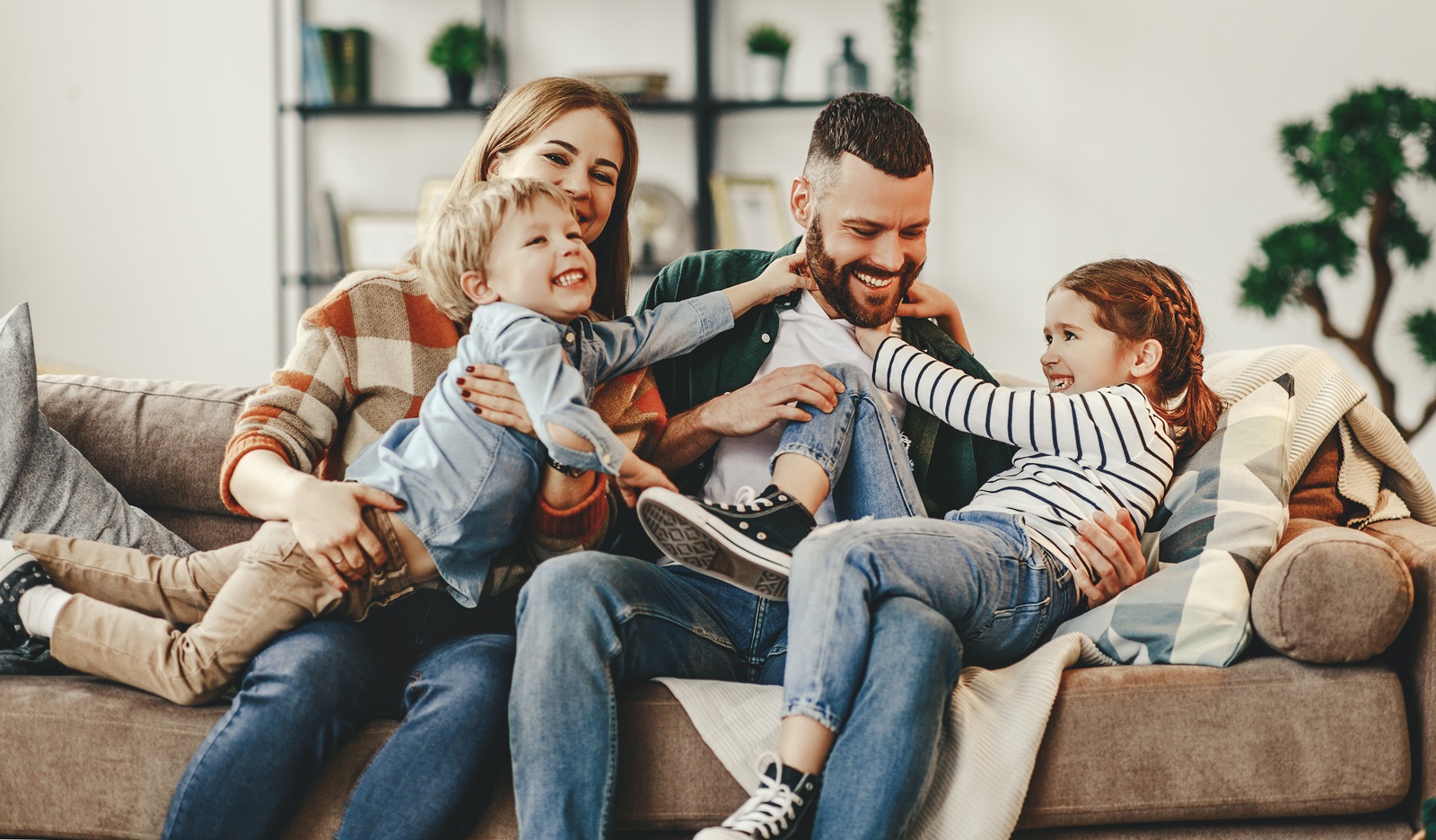 A young couple is on the sofa while their children climb on top of them.