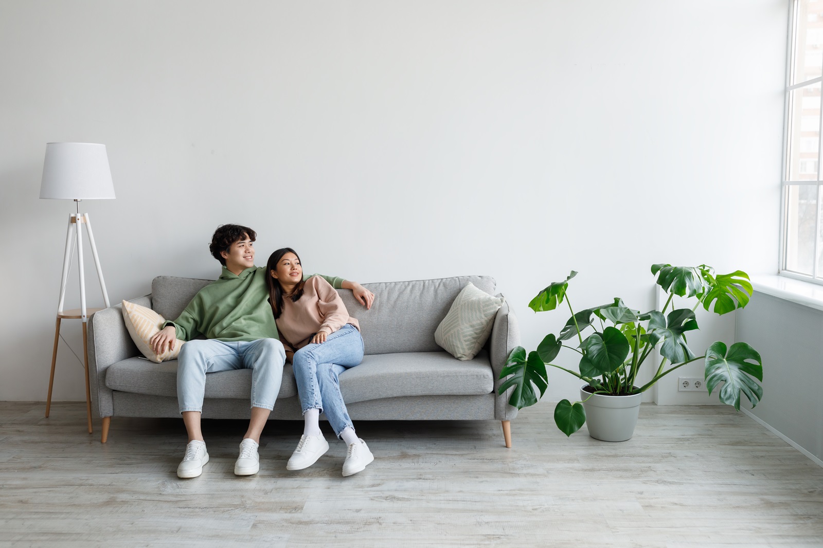 A young couple sit together, looking out the window of their new apartment.