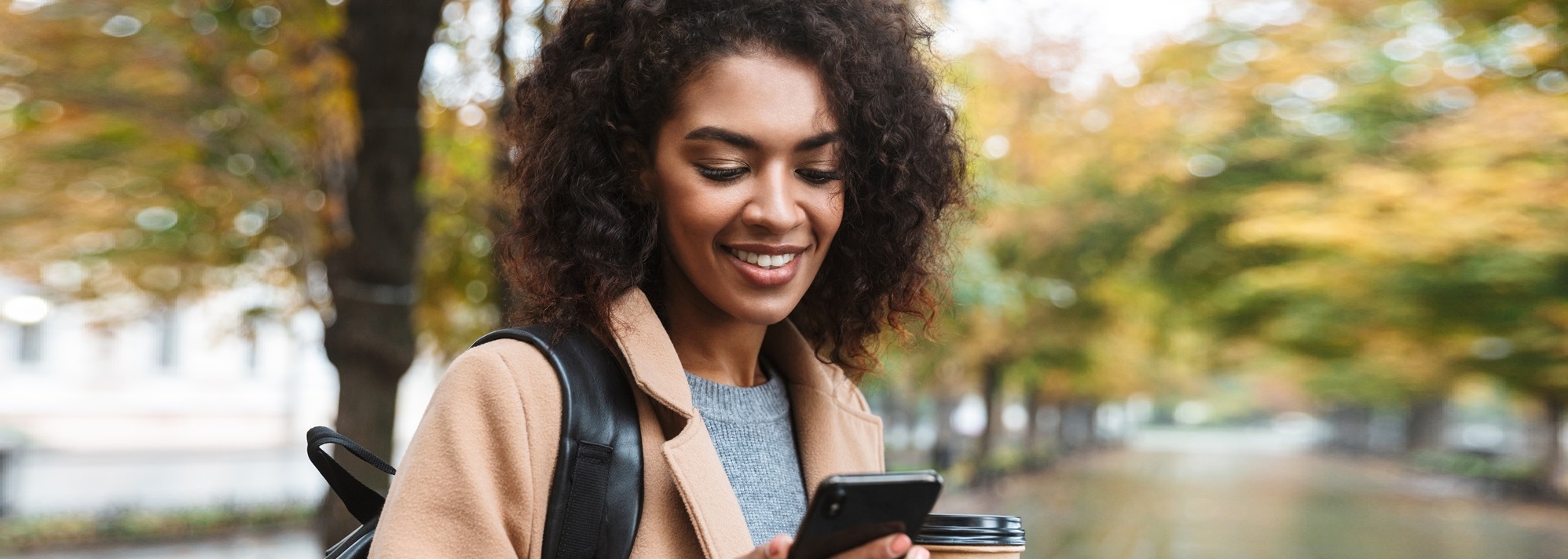 A woman smiling while looking at her phone.